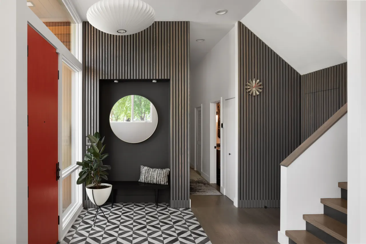 Foyer with slatted wall paneling, round mirror and patterned tile floor