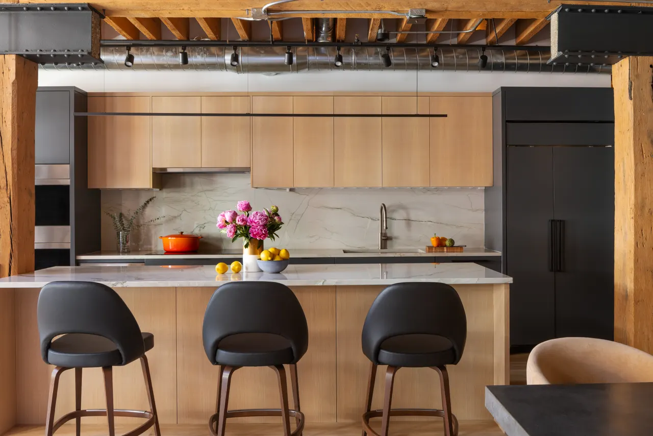 Kitchen with light wood cabinetry, marble backsplash and island seating